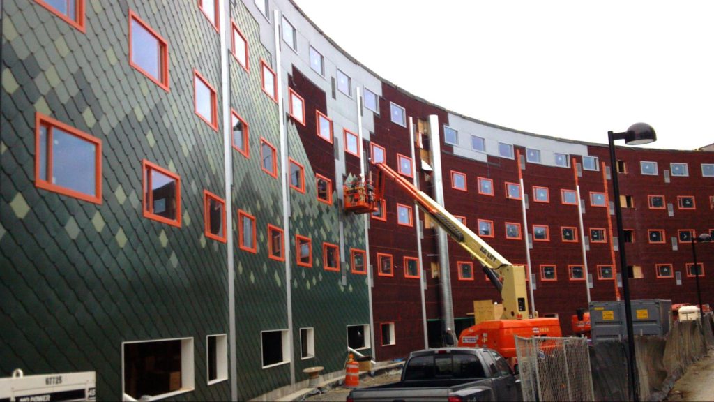 A side view of a commercial building as green cladding is installed, complementing the orange-framed Paradigm windows.