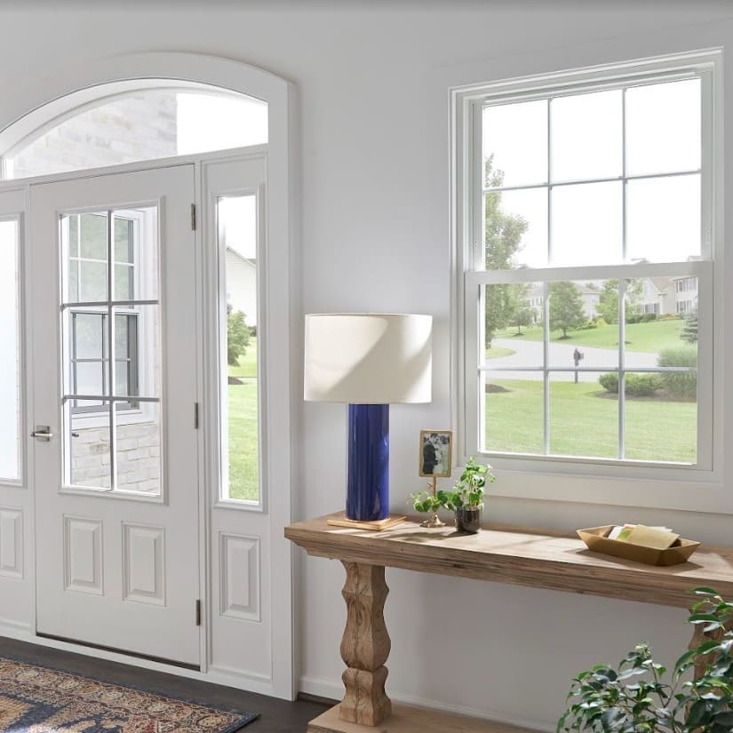 Entryway with white walls and door, wooden entryway table with blue lamp and small plant on the table. 