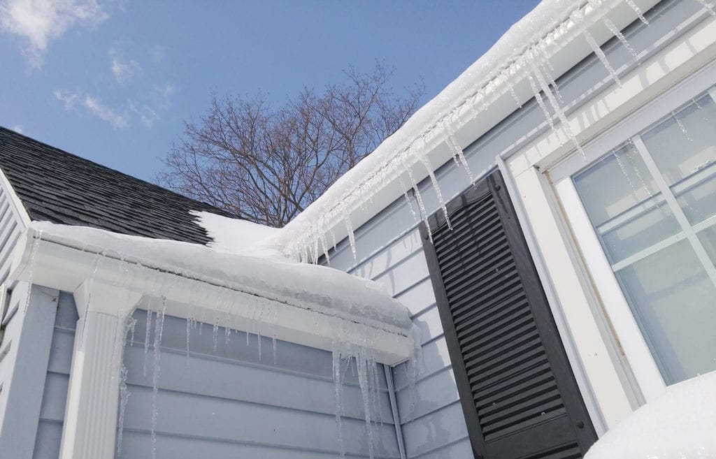 Looking up at the gutters which have snow and icicles hanging from them, and a blue sky above.