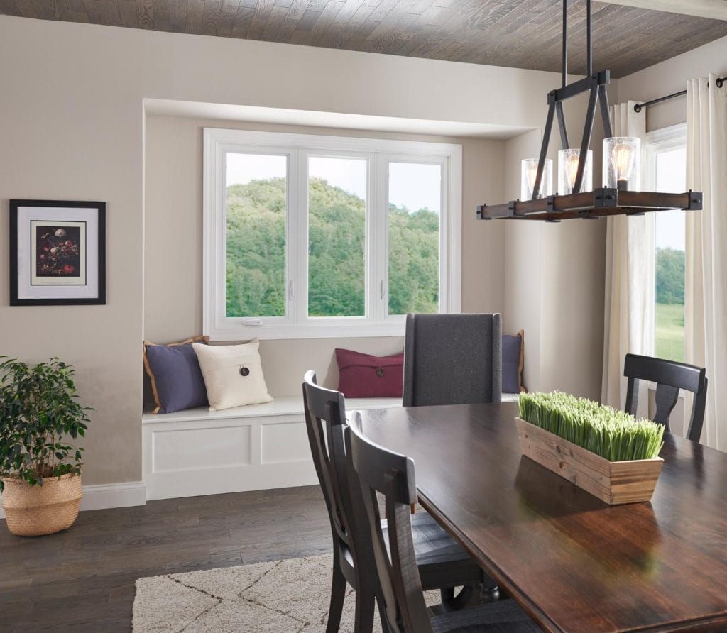 A stylish dining room with a dark wood table, farmhouse overhead light fixture and window seat with pillows.